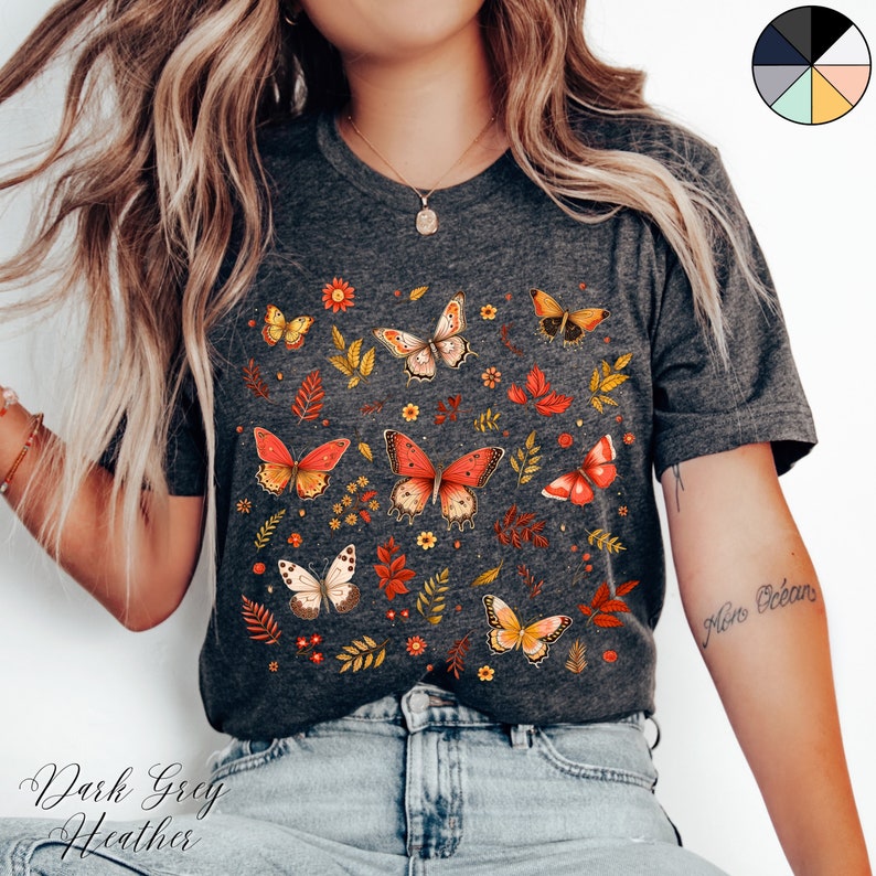 May include: A dark grey heather t-shirt with a print of colorful butterflies and leaves. The shirt has a crew neck and short sleeves.