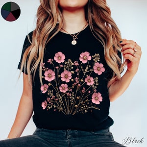Pu&ograve; includere: Una maglietta nera con un design floreale con fiori rosa e steli dorati. I fiori sono disposti a forma di bouquet.