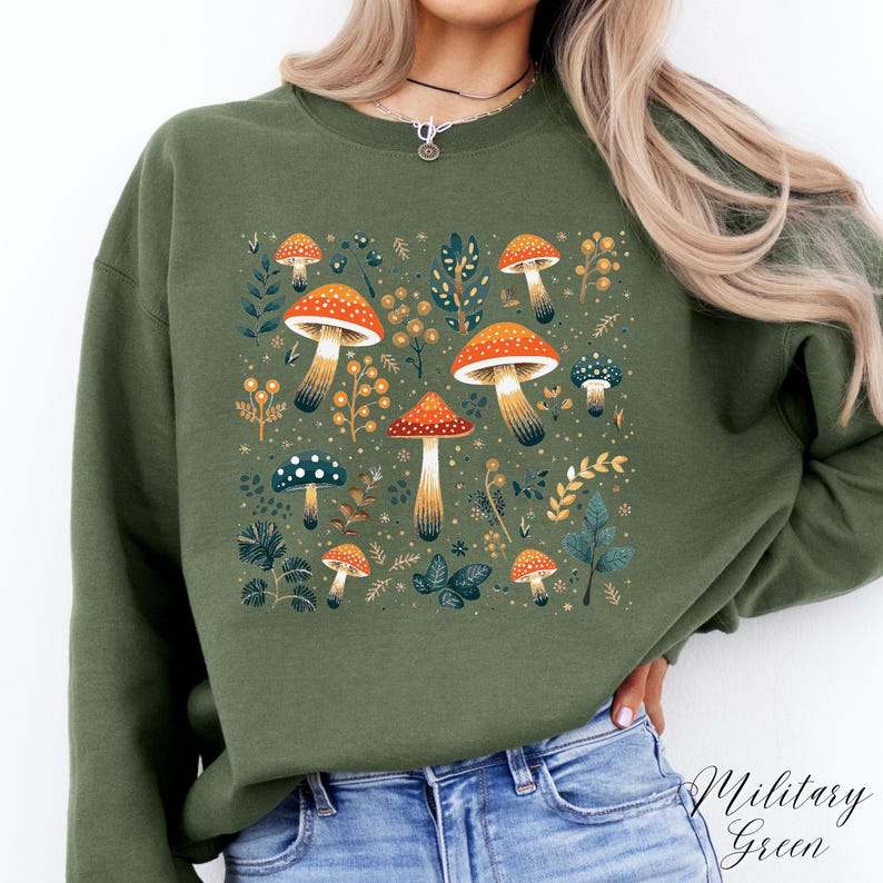 May include: A green sweatshirt with a mushroom and leaf design. The mushrooms are red and white with brown stems. The leaves are green and yellow.