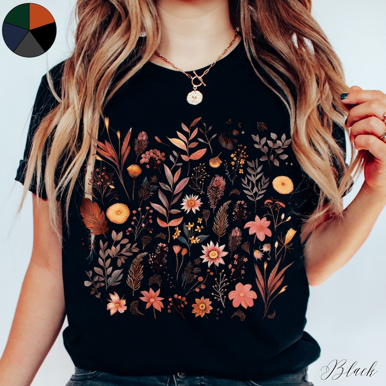 K&ouml;nnte beinhalten: Schwarzes T-Shirt mit einem floralen Druck, der verschiedene Blumen und Bl&auml;tter in Orange-, Braun- und Rosat&ouml;nen zeigt.