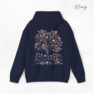 Peut inclure: Un sweat &agrave; capuche bleu marine avec un motif d'arbre floral au dos. L'arbre est de couleur brun clair avec des fleurs roses, orange et bleues.