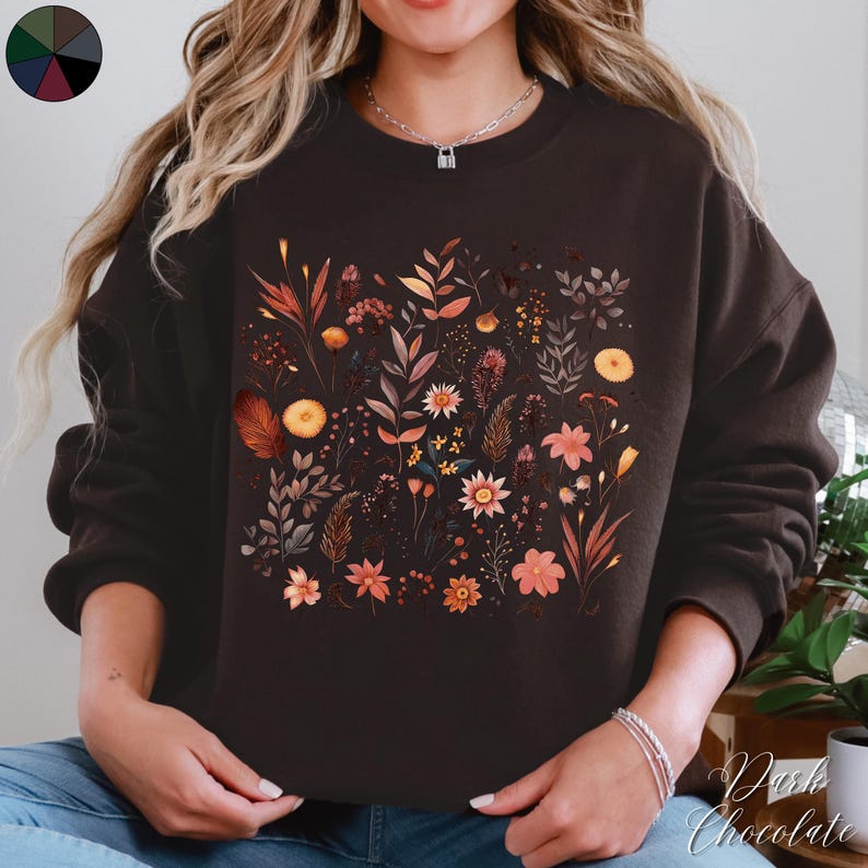 May include: A brown sweatshirt with a floral print featuring various shades of orange, yellow, and pink. The flowers are arranged in a random pattern and are surrounded by green leaves.