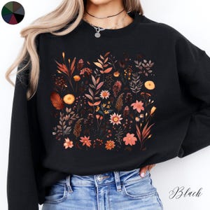 May include: Black sweatshirt with a floral print featuring a variety of flowers and leaves in shades of orange, brown, and yellow.