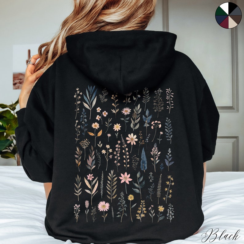 May include: Black hooded sweatshirt with a floral print on the back. The print features a variety of flowers and leaves in shades of pink, yellow, and green.