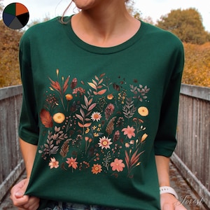 K&ouml;nnte beinhalten: Ein dunkelgr&uuml;nes T-Shirt mit einem Blumendruck in verschiedenen Oranget&ouml;nen, Gelb- und Rosat&ouml;nen. Die Blumen sind in einer Gruppe auf der Vorderseite des Shirts angeordnet.