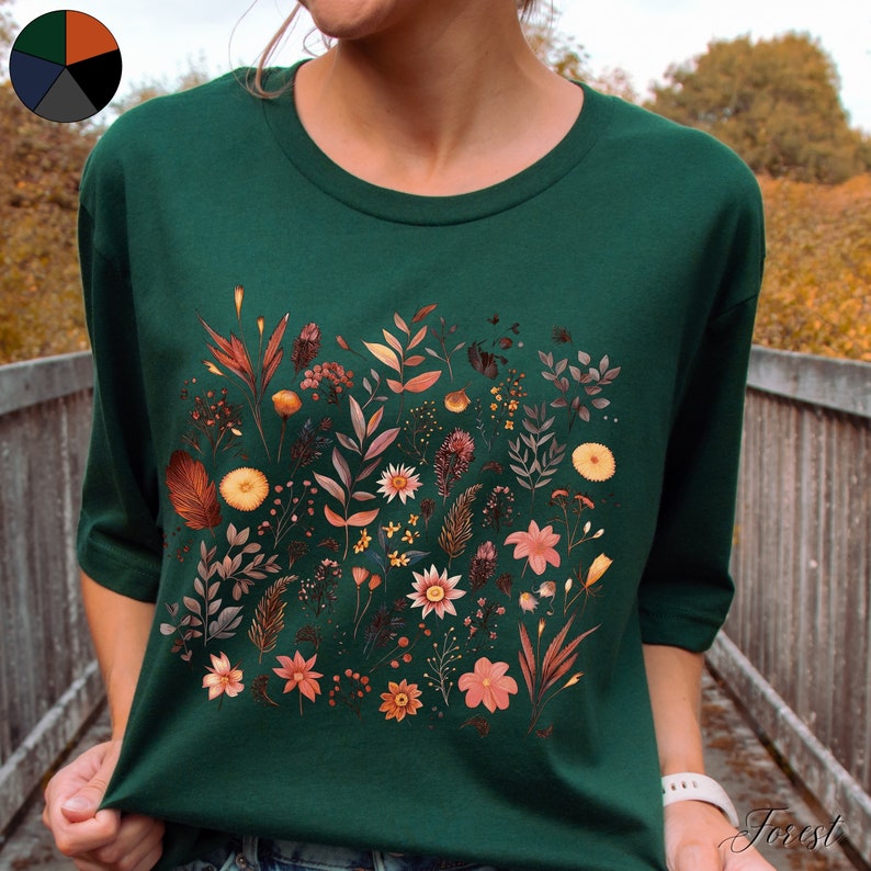 K&ouml;nnte beinhalten: Ein dunkelgr&uuml;nes T-Shirt mit einem Blumendruck in verschiedenen Oranget&ouml;nen, Gelb- und Rosat&ouml;nen. Die Blumen sind in einer Gruppe auf der Vorderseite des Shirts angeordnet.