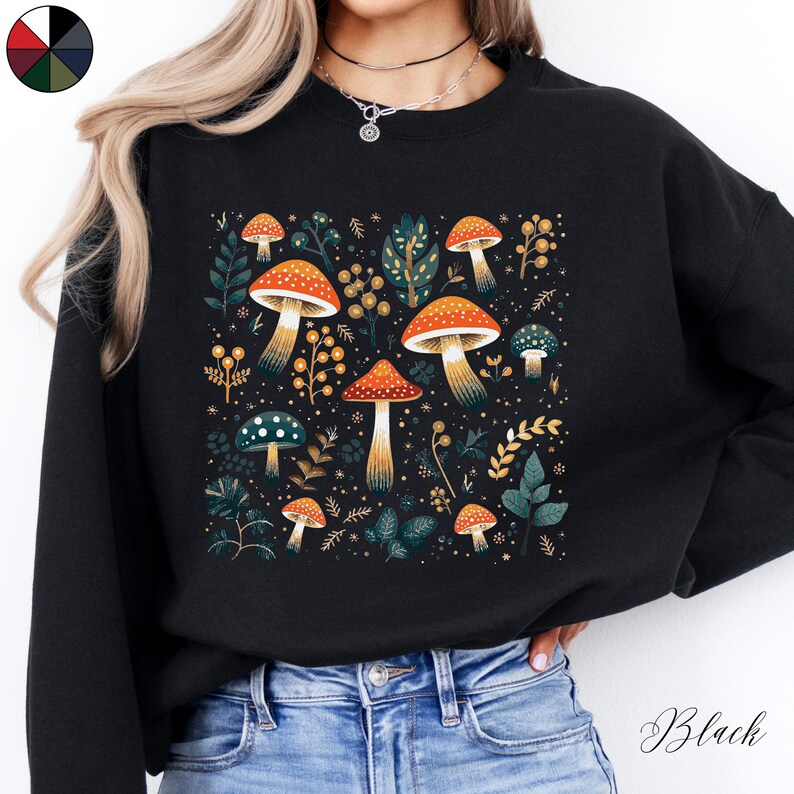 May include: Black sweatshirt with a colorful mushroom and floral print. The print features a variety of mushrooms in different colors and sizes, surrounded by leaves and flowers.