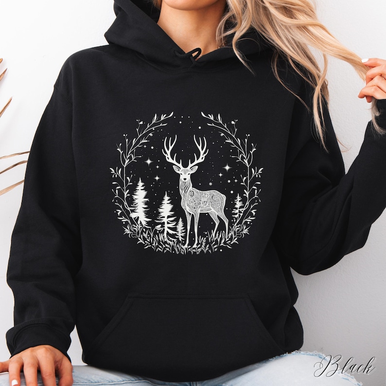 May include: Black hoodie featuring a white illustration of a deer with intricate patterns, surrounded by a forest scene with trees, stars, and foliage. The word "Black" is written in cursive at the bottom right.