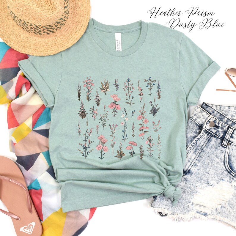 May include: A light blue t-shirt with a floral print featuring a variety of pink and blue flowers. The shirt is made of a soft, comfortable material and has a relaxed fit.