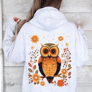May include: A gray hoodie with a graphic of an orange and brown owl sitting on a branch with orange flowers. The owl has a detailed pattern on its feathers.