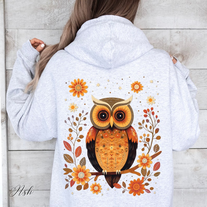 May include: A gray hoodie with a graphic of an orange and brown owl sitting on a branch with orange flowers. The owl has a detailed pattern on its feathers.