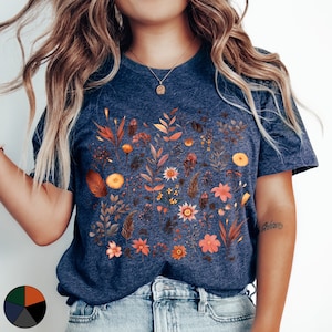 K&ouml;nnte beinhalten: Ein marineblaues T-Shirt mit einem Blumenmuster, das verschiedene Blumen und Bl&auml;tter in Orange-, Gelb- und Rosat&ouml;nen zeigt. Das Shirt hat einen Rundhalsausschnitt und kurze &Auml;rmel.