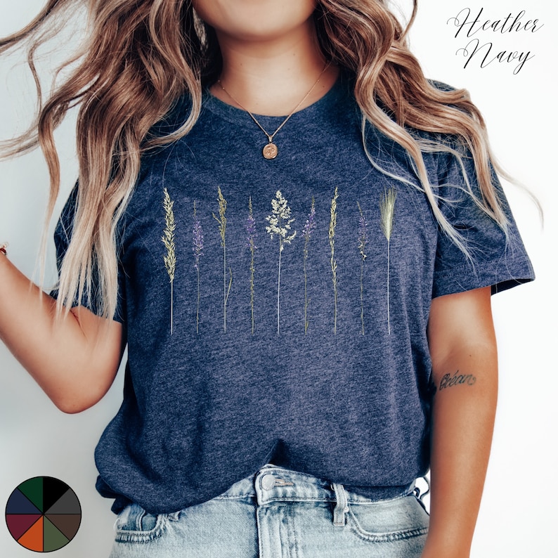 May include: A heather navy blue t-shirt featuring a graphic of a row of dried grasses and flowers. The shirt has a crew neck and short sleeves.