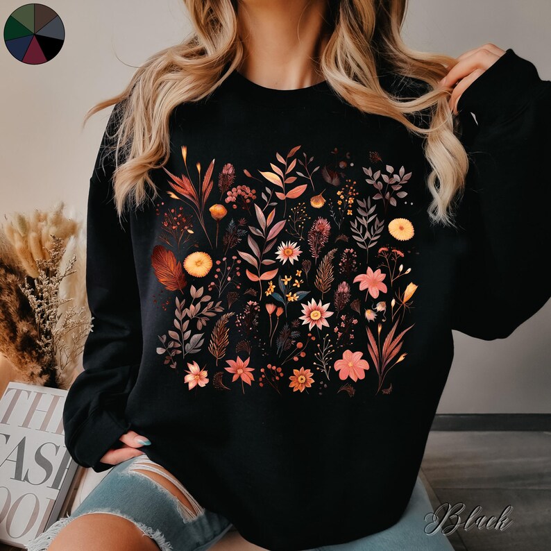 May include: Black sweatshirt with a floral print featuring various shades of orange, red, and yellow flowers. The flowers are arranged in a cluster on the front of the sweatshirt.