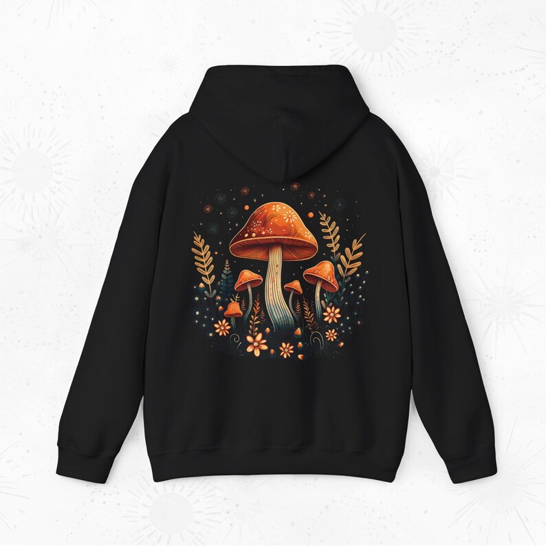 Op de afbeelding: Zwarte hoodie met een kleurrijk paddenstoelontwerp. Het ontwerp toont oranje en witte paddenstoelen, omringd door bloemen en bladeren. De hoodie heeft een capuchon en lange mouwen.