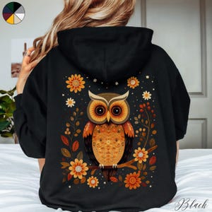 May include: Black hoodie with a colorful owl and floral design on the back. The owl has orange, brown, and yellow feathers. The flowers are yellow, orange, and white.