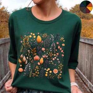 Może przedstawiać: Zielony T-shirt z nadrukiem kwiatowym przedstawiającym r&oacute;żne kwiaty w odcieniach ż&oacute;łtego, pomarańczowego, r&oacute;żowego i fioletowego. Kwiaty są ułożone w kwadratowy wz&oacute;r na przodzie koszulki.