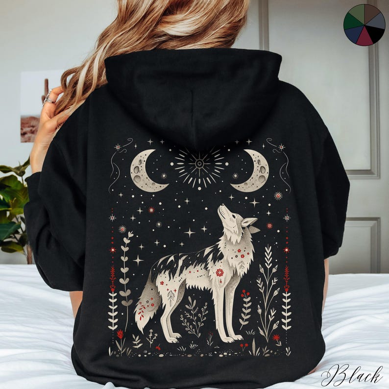 May include: Black hooded sweatshirt with a graphic print of a wolf howling at the moon. The design features a starry night sky with crescent moons and floral accents.
