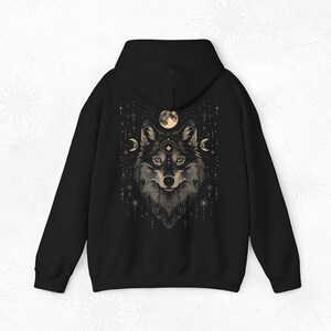 K&ouml;nnte beinhalten: Schwarzer Kapuzenpullover mit einem grafischen Aufdruck eines Wolfskopfes mit einem Mond und Sternen im Hintergrund.