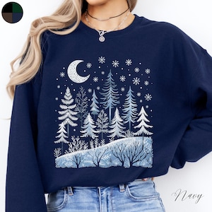 May include: Navy blue sweatshirt with a winter forest scene printed on the front. The design features a crescent moon, snow-covered trees, and snowflakes.