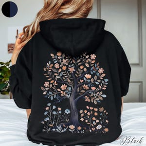 Peut inclure: Sweat-shirt &agrave; capuche noir avec un motif d'arbre floral au dos. L'arbre est de couleur gris fonc&eacute; avec des fleurs roses et bleues.