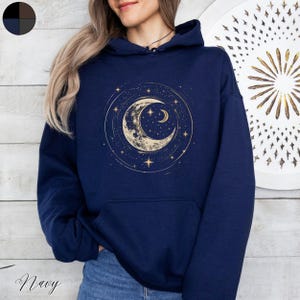 Op de afbeelding: Een marineblauwe hoodie met een gouden halve maan en sterren print. De hoodie heeft een capuchon met trekkoord en een kangoeroezak.