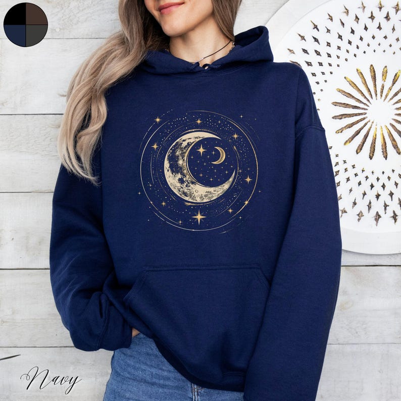 Op de afbeelding: Een marineblauwe hoodie met een gouden halve maan en sterren print. De hoodie heeft een capuchon met trekkoord en een kangoeroezak.