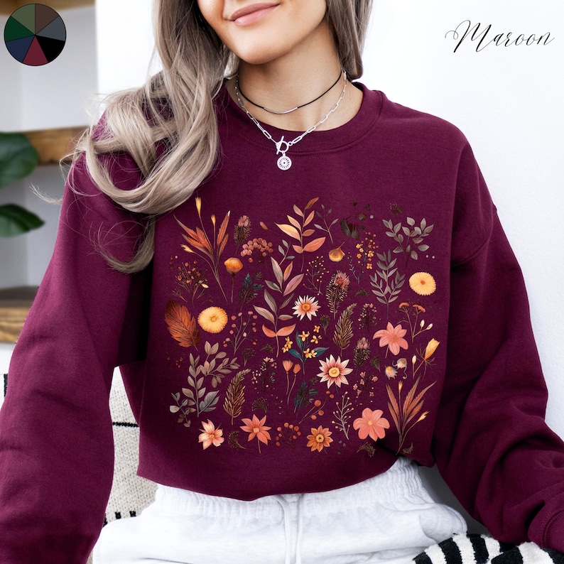 May include: A maroon cropped sweatshirt with a floral print featuring various shades of brown, orange, and yellow flowers. The text "Maroon" is visible in the top right corner of the image.