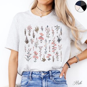 May include: A grey t-shirt with a floral print featuring pink and blue flowers. The shirt has a crew neck and short sleeves.