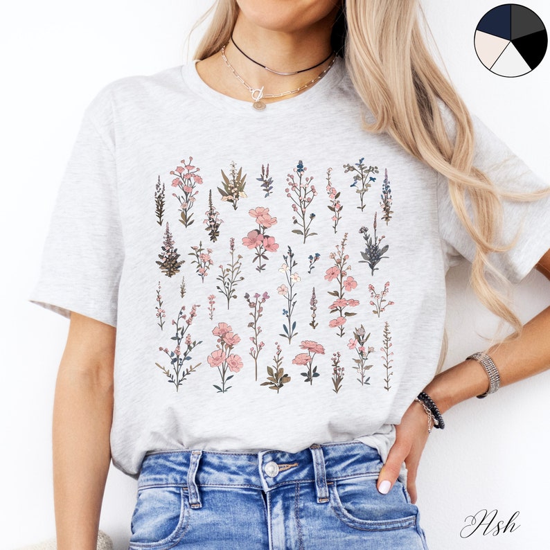 May include: A grey t-shirt with a floral print featuring pink and blue flowers. The shirt has a crew neck and short sleeves.