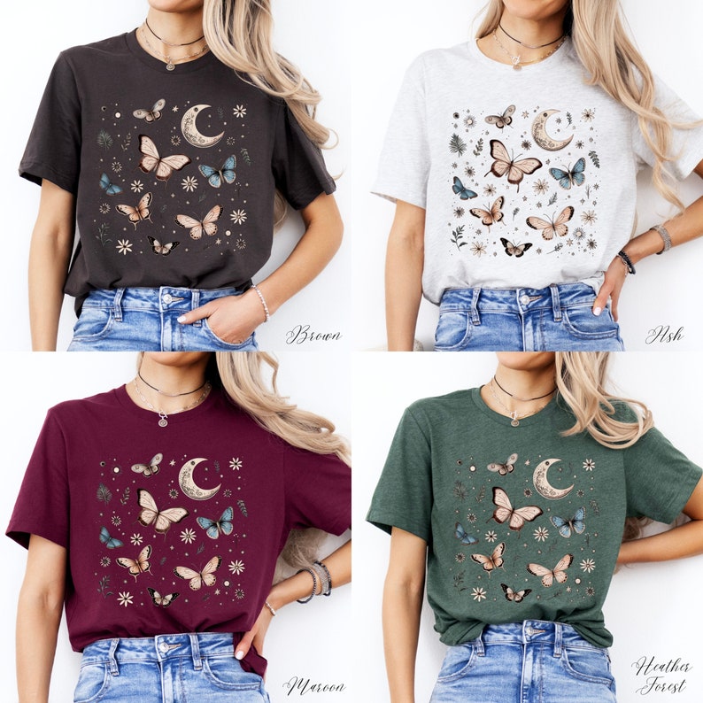 May include: Four different color t-shirts featuring a graphic print of butterflies, a crescent moon, and floral elements. The colors are brown, ash, maroon, and heather forest.