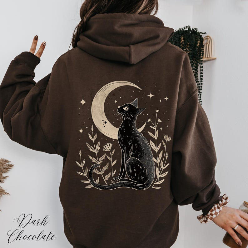 May include: A brown hoodie with a black cat silhouette design on the back. The cat is looking up at a crescent moon with stars in the background. The design is surrounded by stylized plants.