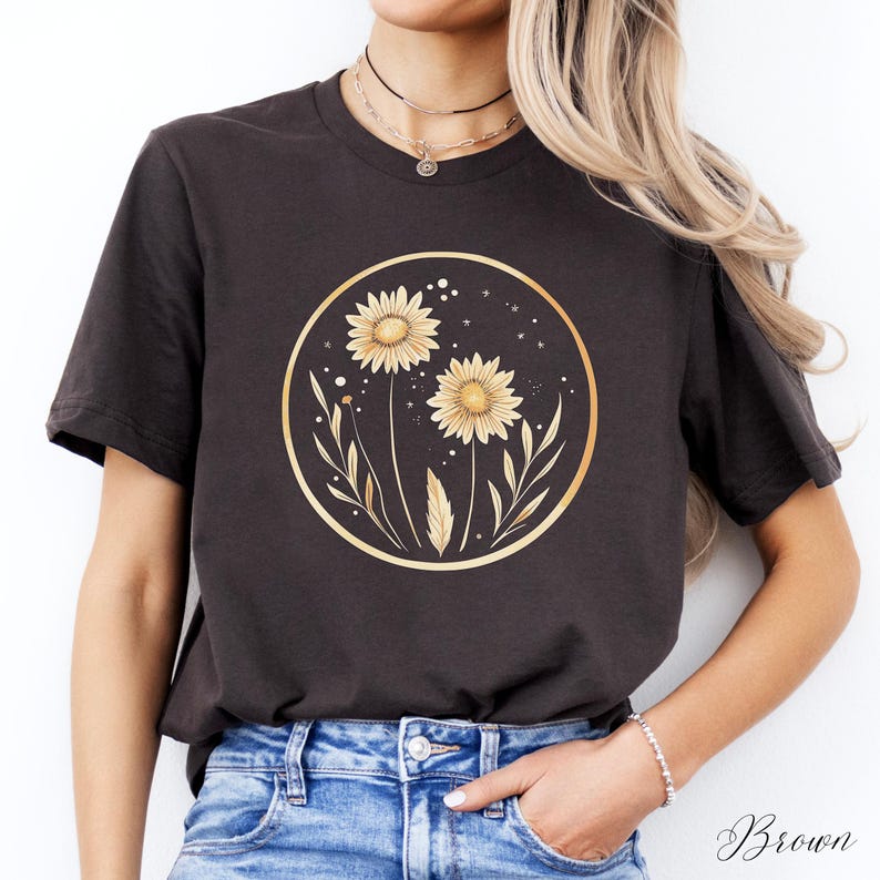 May include: Brown t-shirt featuring a gold circular design with two yellow sunflowers and leaves. The design is centered on the shirt. The word "Brown" is written in cursive at the bottom right of the image.