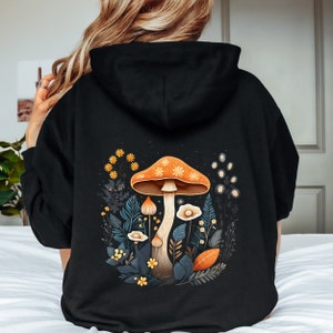 May include: Black hooded sweatshirt with a graphic print of orange and yellow mushrooms and flowers on the back.