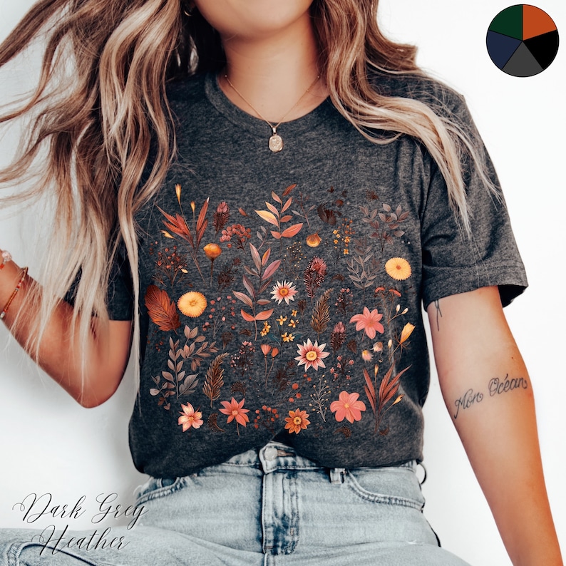 K&ouml;nnte beinhalten: Ein dunkelgraues Heather-T-Shirt mit einem floralen Druck in verschiedenen Oranget&ouml;nen, Gelb und Rosa. Der Druck ist ein Muster aus Bl&auml;ttern und Blumen. Das Shirt hat einen Rundhalsausschnitt und kurze &Auml;rmel.