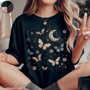 May include: A black t-shirt with a moon and butterfly design. The butterflies are in shades of blue, white, and brown. The moon is crescent shaped and has a floral design.