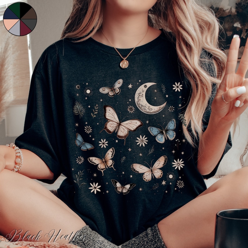 May include: A black t-shirt with a moon and butterfly design. The butterflies are in shades of blue, white, and brown. The moon is crescent shaped and has a floral design.