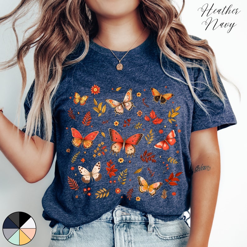 May include: A heather navy blue t-shirt with a colorful butterfly and floral print. The print features orange, yellow, and white butterflies on a background of green leaves and yellow flowers.