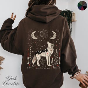 May include: A brown hooded sweatshirt with a graphic print of a wolf howling at the moon. The print also includes stars, flowers, and a crescent moon.