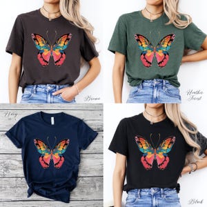 Pu&ograve; includere: Quattro t-shirt a maniche corte in marrone, verde foresta melange, blu navy e nero. Ogni maglietta presenta una grafica a farfalla colorata sul davanti. Il design della farfalla include sfumature di rosso, arancione, giallo, blu e verde.