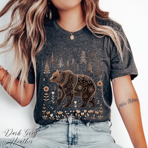 May include: Dark grey heather t-shirt featuring a detailed brown bear design with floral and tree accents. The bear is adorned with intricate patterns. The text "Dark Grey Heather" is printed at the bottom of the shirt.