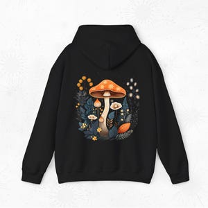 May include: Black hooded sweatshirt featuring a printed design of a mushroom with orange and yellow accents, surrounded by flowers and leaves.