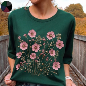 Pu&ograve; includere: Una maglietta verde con una stampa floreale di fiori rosa e steli marroni.