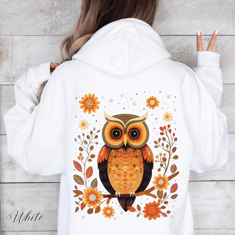 May include: White hooded sweatshirt with a brown and orange owl design on the back. The owl is surrounded by flowers and leaves in shades of orange, yellow, and brown.