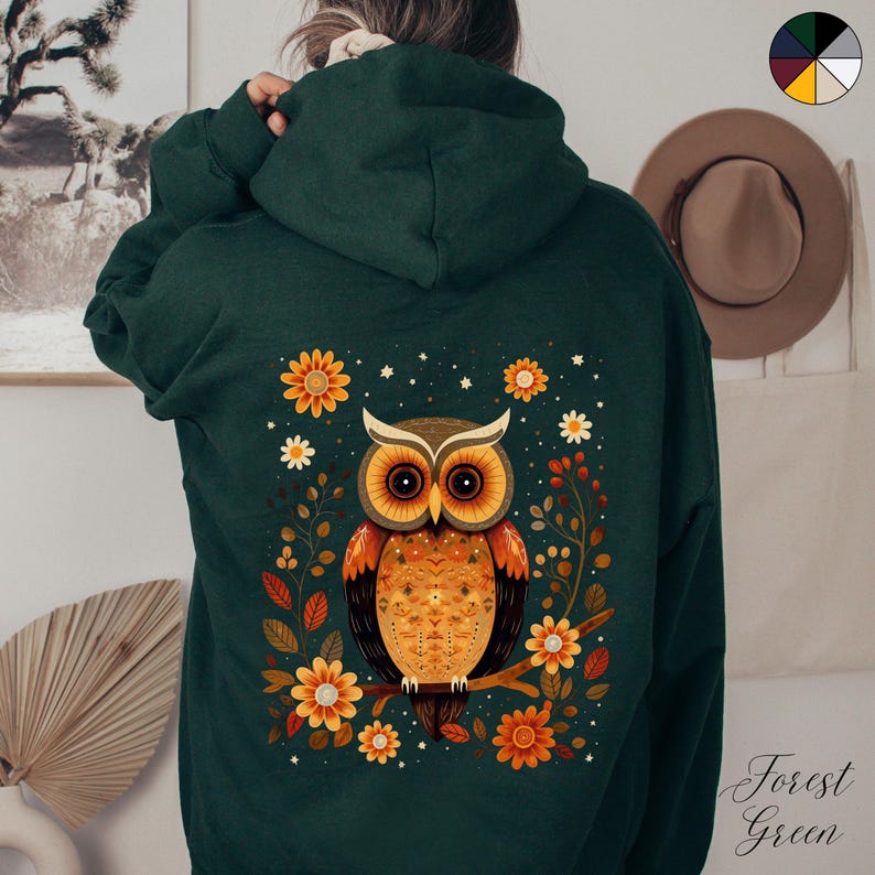 May include: A forest green hoodie with a colorful owl and floral design on the back. The owl has orange, yellow, and brown feathers and large, black eyes. The flowers are yellow, orange, and white.