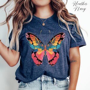 Pu&ograve; includere: T-shirt blu navy con un design a farfalla colorato. La farfalla presenta un motivo astratto nei toni del rosa, arancione, giallo e blu. La maglietta ha maniche corte e girocollo. Il testo "Heather Navy" &egrave; visibile.