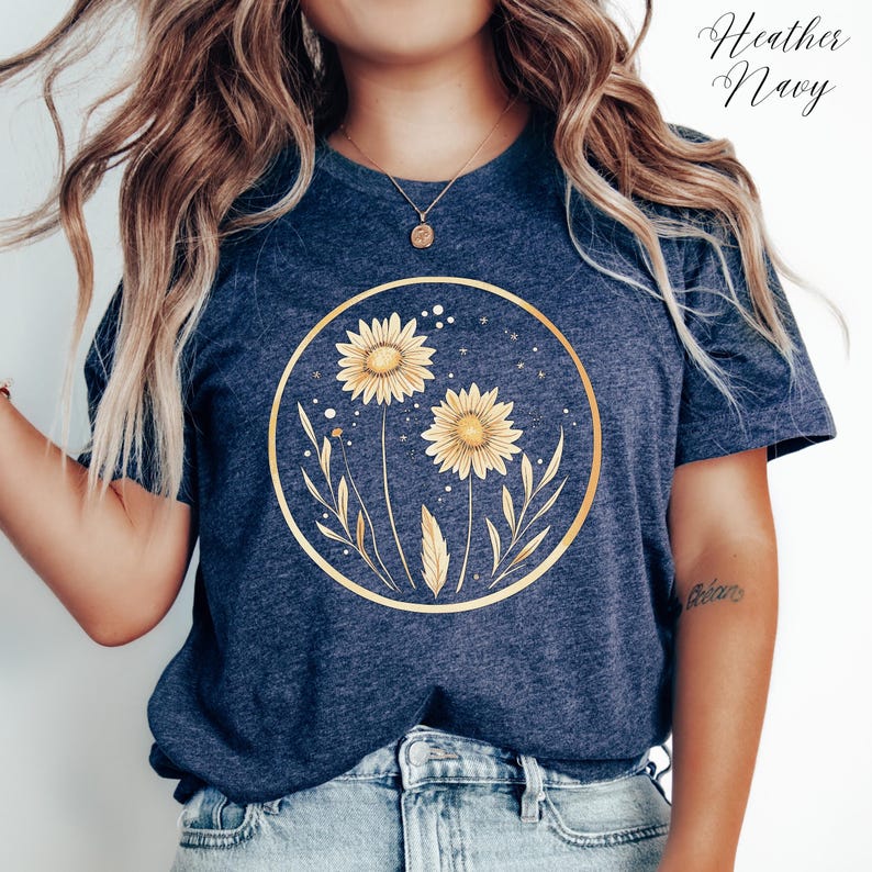 May include: Heather Navy t-shirt featuring a gold circular design with two sunflowers and leaves. The sunflowers have yellow petals and are surrounded by a gold outline. The text "Heather Navy" is written in cursive at the top right.