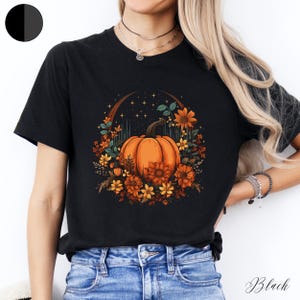 May include: Black t-shirt featuring a graphic of an orange pumpkin surrounded by autumnal flowers and a crescent moon with stars.
