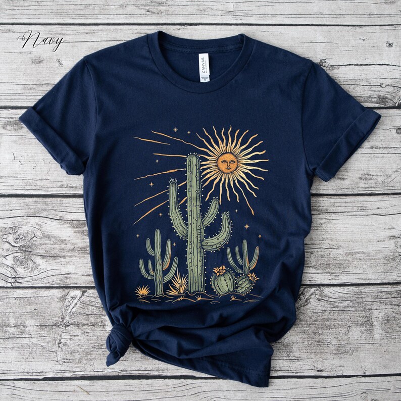 May include: Navy blue t-shirt featuring a desert scene with cacti and a smiling sun graphic. The design includes various cacti in shades of green and yellow, with a radiant sun and stars. The shirt is made of a soft material.