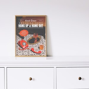 May include: A framed print with a vintage newspaper design. The headline reads "Good Times Breaking News Hang Up & Hang Out". The image features a red rotary phone, a glass of red wine, and a glass of whisky on a patterned surface.
